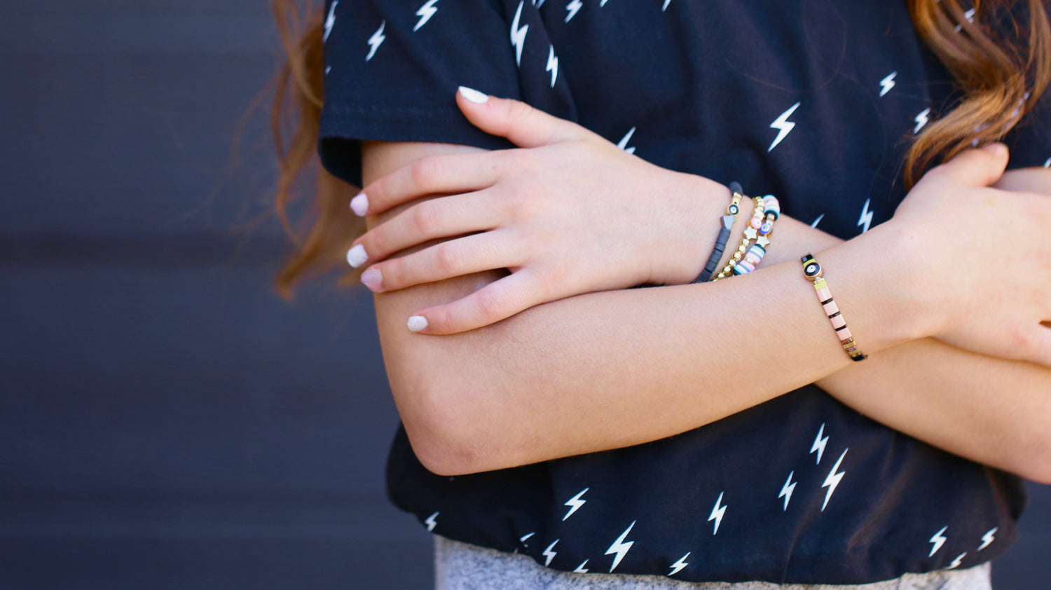 image highlighting the bracelets on a young girls arm. she has them crisscrossed against her black shirt with white lighting bolts across.