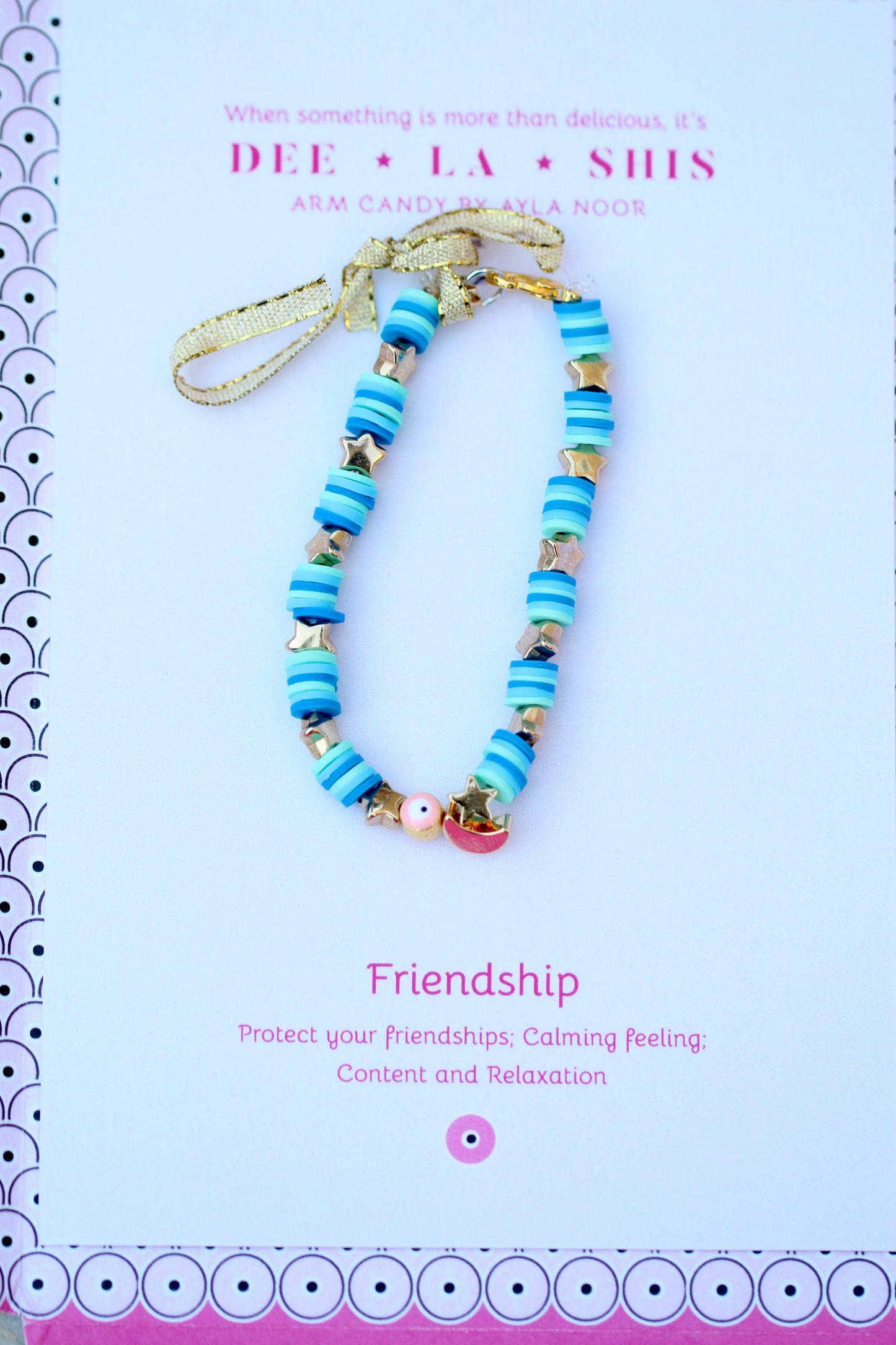 Bright blue bracelet on fun pink packaging tied with a gold ribbon