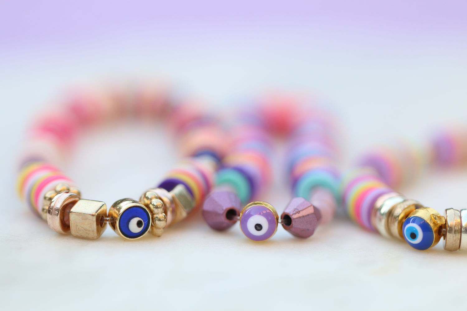 zoomed in image of 3 bracelets in bright pink purple and blue colors with an evil eye in blue and purple in the middle of each bracelet