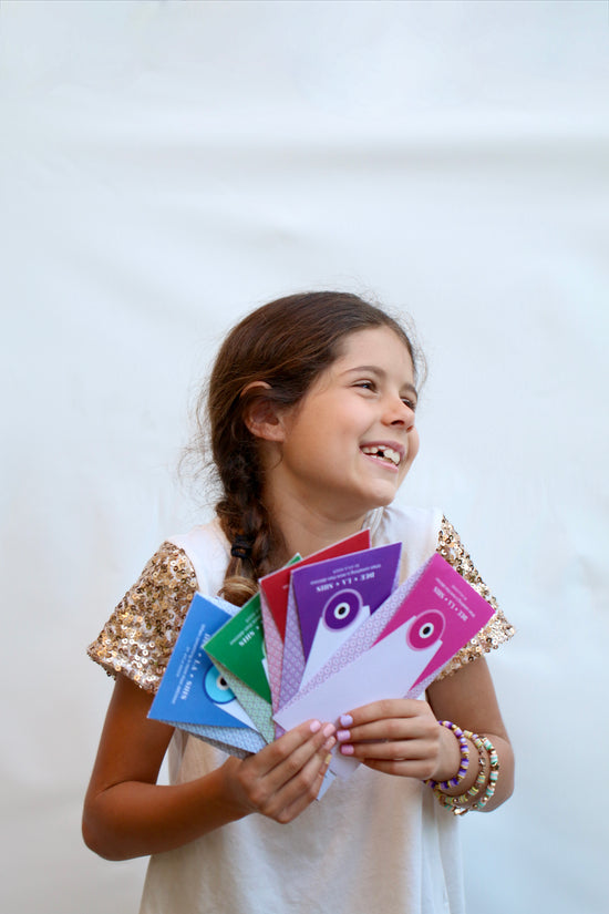 An 8 year old girl looking over to the left and smiling while holding colorful packages and a brown braid in her hair
